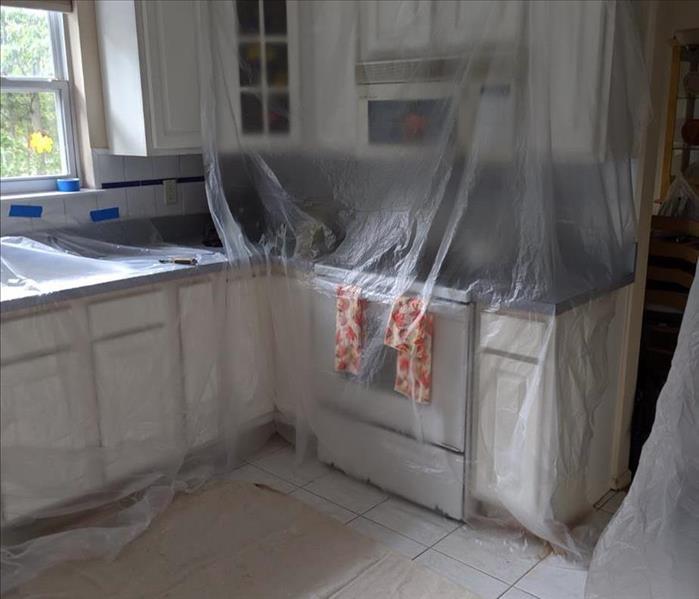 Kitchen with white wood cabinets with taped up plastic barriers for protection 